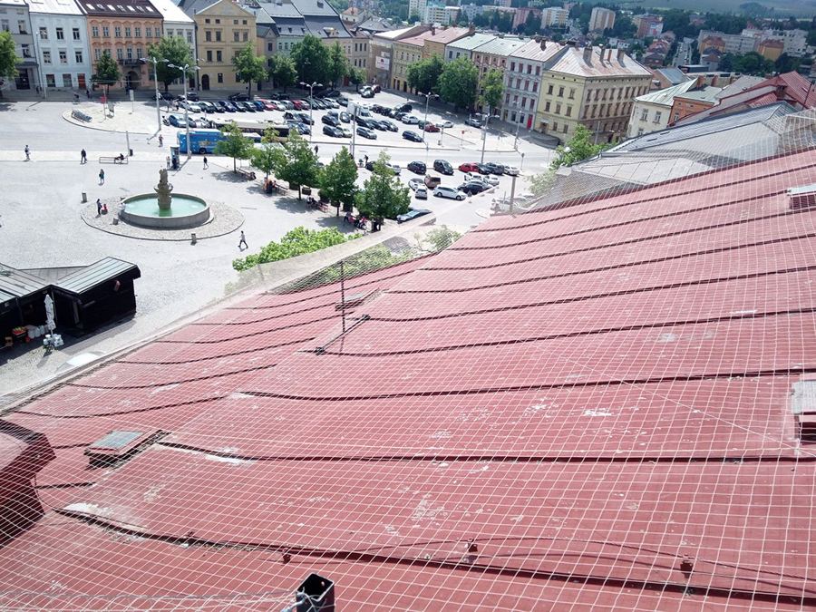 Síť napnutá nad střešní plochou, v pozadí historické náměstí